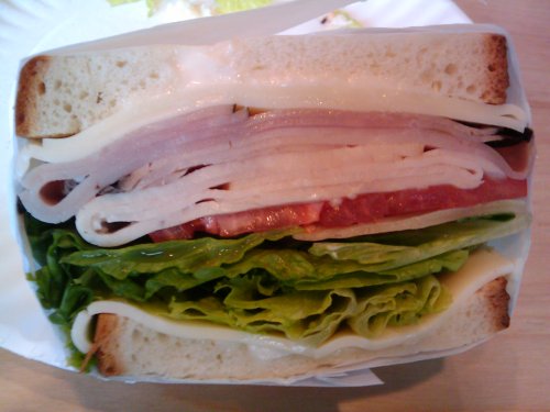 A cross-section of a sandwich with layers of lettuce, tomato, ham, and cheese between two slices of bread.