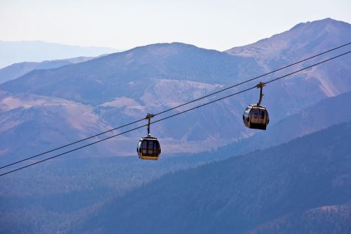 Two gondolas suspended on a cable above a mountainous landscape with blue skies in the background.