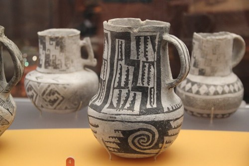 Four decorative pottery vessels with intricate black and white patterns displayed on a shelf.