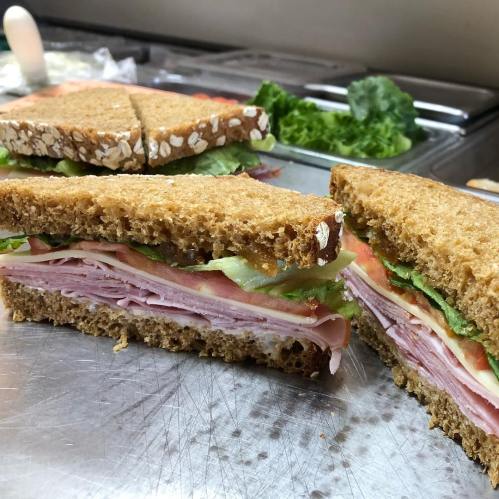 A freshly made sandwich with layers of ham, turkey, lettuce, and tomato, served on whole grain bread.