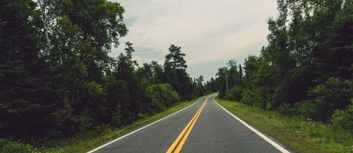 A winding road surrounded by lush green trees under a cloudy sky.