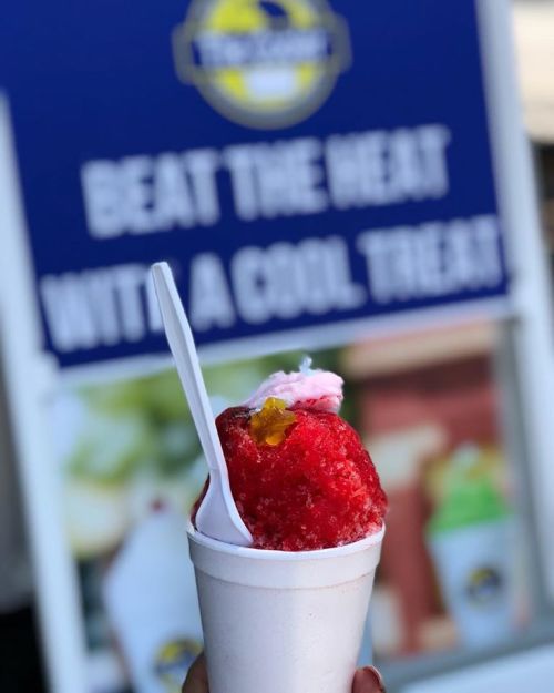 A colorful snow cone in a cup with a spoon, set against a sign promoting cool treats.
