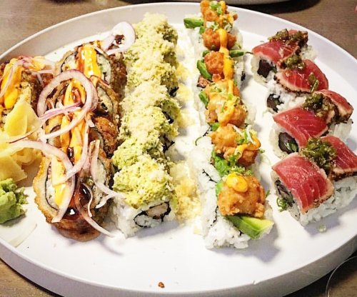 A platter of assorted sushi rolls, including tuna, tempura, and avocado, garnished with sauces and vegetables.