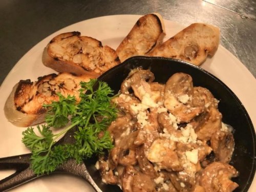 A cast iron skillet with creamy mushrooms and cheese, accompanied by toasted bread slices and a sprig of parsley.