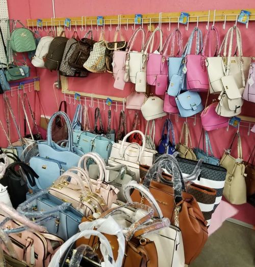 A variety of handbags in different colors and styles hanging on display against a pink wall.