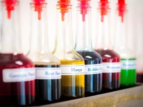 A row of colorful glass bottles filled with various flavored syrups, each labeled with its flavor.