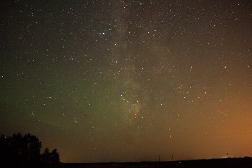 A starry night sky with the Milky Way visible, illuminated by soft hues of light from the horizon.