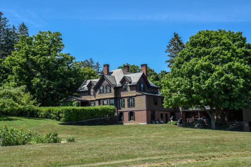 A large, historic house surrounded by lush green trees and a grassy lawn under a clear blue sky.