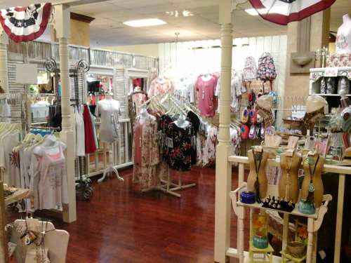 A boutique interior featuring clothing racks, accessories, and a warm, inviting atmosphere with wooden decor.
