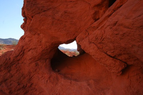 A natural rock formation with a circular opening, framed by red sandstone, revealing distant mountains beyond.