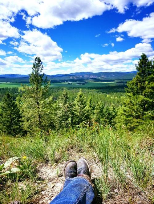 A pair of boots resting on a grassy hillside, overlooking a lush green valley and blue sky with fluffy clouds.