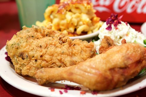 A plate of crispy fried chicken, macaroni and cheese, and a side salad, served with a drink in the background.