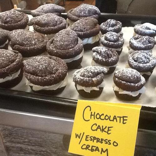 A display of chocolate cakes and cupcakes topped with powdered sugar, labeled "Chocolate Cake w/ Espresso Cream."