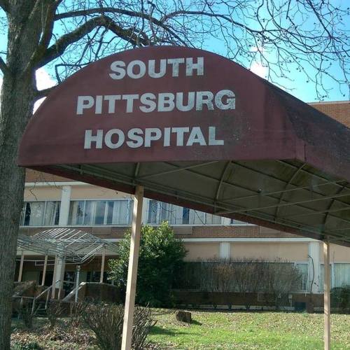 Sign for South Pittsburg Hospital under a canopy, with trees and a building in the background.