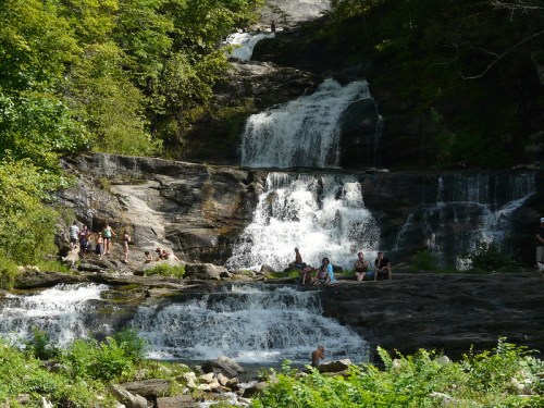 A scenic waterfall with multiple tiers, surrounded by lush greenery and people enjoying the natural beauty.