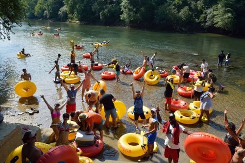 A lively river scene with people in colorful inner tubes, enjoying a sunny day and splashing in the water.
