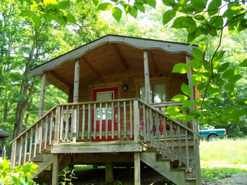 A cozy wooden cabin with a red door, surrounded by lush greenery and trees.