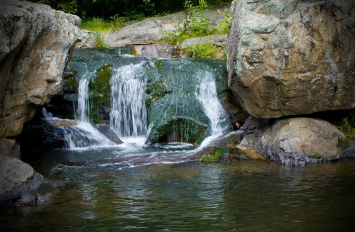 A serene waterfall cascading over moss-covered rocks into a calm pool of water surrounded by greenery.