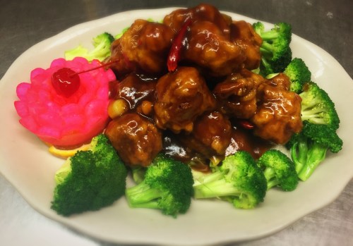 A plate of broccoli topped with sweet and sour chicken, garnished with a pink flower and a cherry.