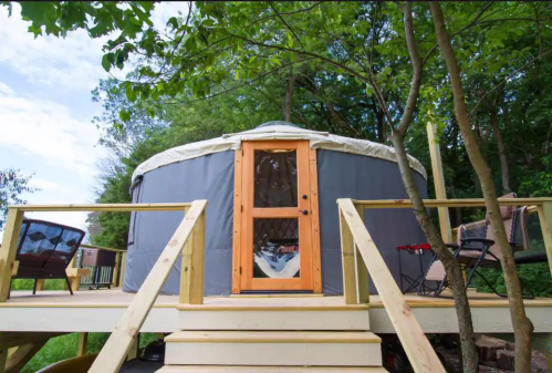 A cozy yurt on a wooden deck surrounded by trees, featuring a wooden door and outdoor seating.
