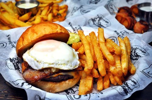 A juicy burger topped with a fried egg, bacon, and onions, served with crispy French fries on the side.