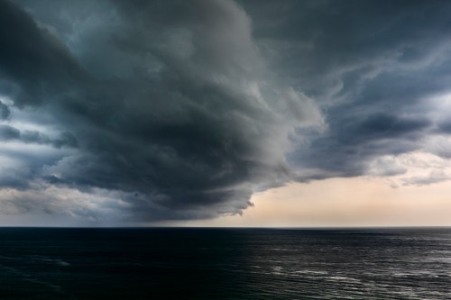 Dark, ominous clouds gather over a calm ocean, hinting at an approaching storm.