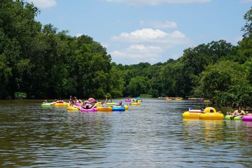 People floating on colorful inner tubes in a river surrounded by lush greenery and blue skies.