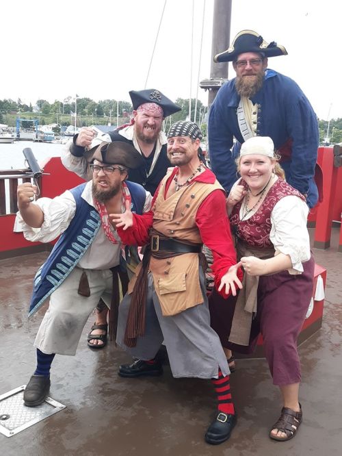 A group of five pirates in costume poses on a ship deck, showcasing their playful expressions and attire.