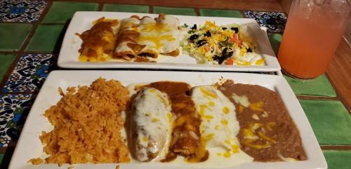 Two plates of Mexican food featuring enchiladas, rice, refried beans, and a side salad, with a drink in the background.