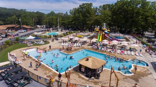 Aerial view of a busy pool area with slides, sunbathers, and lounge chairs surrounded by greenery.