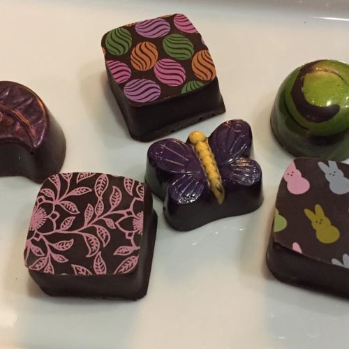 A variety of decorative chocolates with colorful patterns and shapes, including a butterfly and leaf designs.