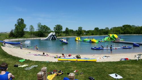 A sunny beach scene with inflatable water slides and play structures, people swimming, and lounging on the shore.