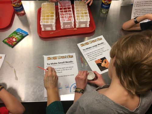 Children participating in a hands-on activity, making colorful beads with instructions and materials on a table.