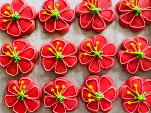 A tray of red flower-shaped cookies decorated with yellow and green icing details.