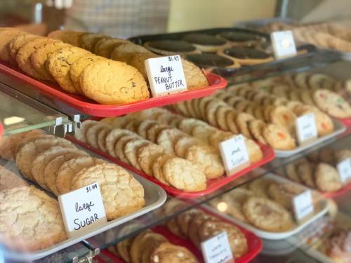 A display case filled with various cookies on red trays, labeled with prices and types like peanut butter and sugar.