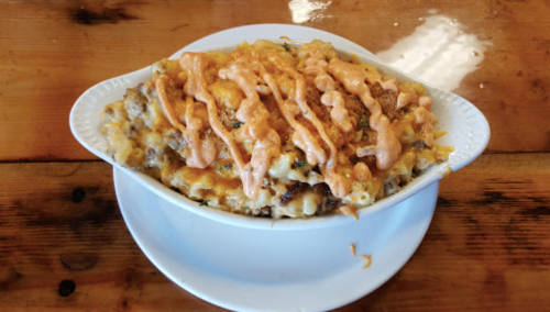 A creamy mac and cheese dish topped with melted cheese and drizzled with a spicy sauce, served in a white bowl.