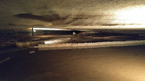 A dimly lit cave interior with a flat, rocky ceiling and a calm water surface reflecting the surroundings.