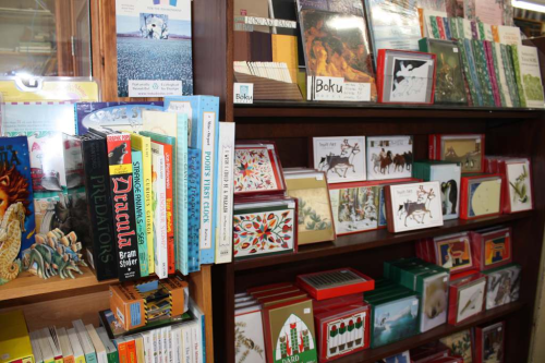 A wooden bookshelf filled with various books and greeting cards, showcasing colorful covers and designs.
