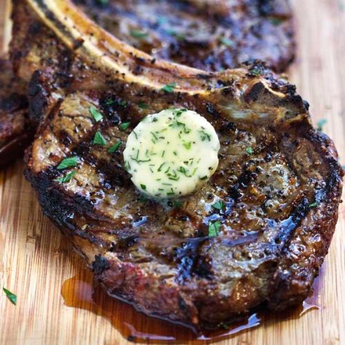 Grilled pork chops topped with a dollop of herb butter, garnished with fresh parsley on a wooden cutting board.