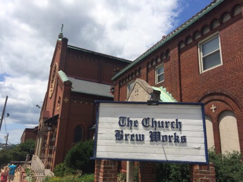 A brick building with a sign reading "The Church Brew Works" under a partly cloudy sky.