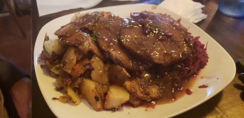 A plate of sliced meat with gravy, served with potatoes and red cabbage.