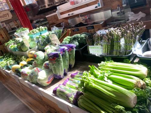 A vibrant display of fresh vegetables, including celery, asparagus, lettuce, and broccoli, at a market stall.