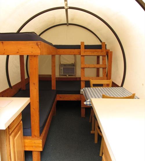 Interior of a cozy cabin with wooden bunk beds, a table with chairs, and an air conditioner.
