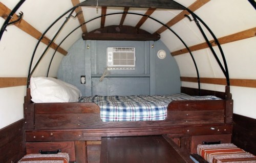 Cozy interior of a small cabin with a bed, air conditioner, and wooden accents.