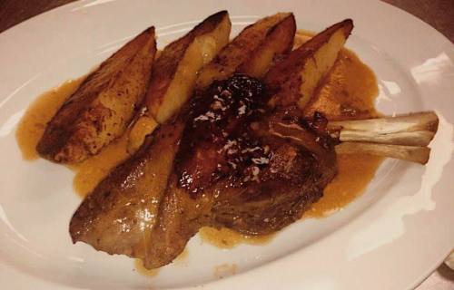 A plate of roasted meat with a rich sauce, accompanied by golden-brown potato wedges.