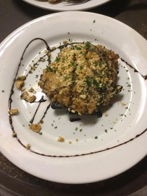 A plated dish featuring a round, breaded and baked item, garnished with crushed nuts and drizzled with sauce.