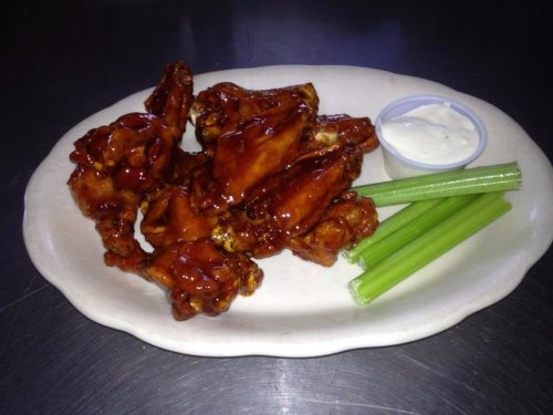 A plate of glazed chicken wings with celery sticks and a side of ranch dressing.