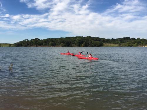 Three people kayaking on a calm lake surrounded by greenery under a partly cloudy sky.