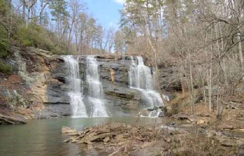 A serene waterfall cascades over rocky cliffs, surrounded by trees and a calm pool of water below.