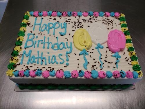 A decorated birthday cake with colorful frosting, balloons, and the message "Happy Birthday Mathias!" written on top.